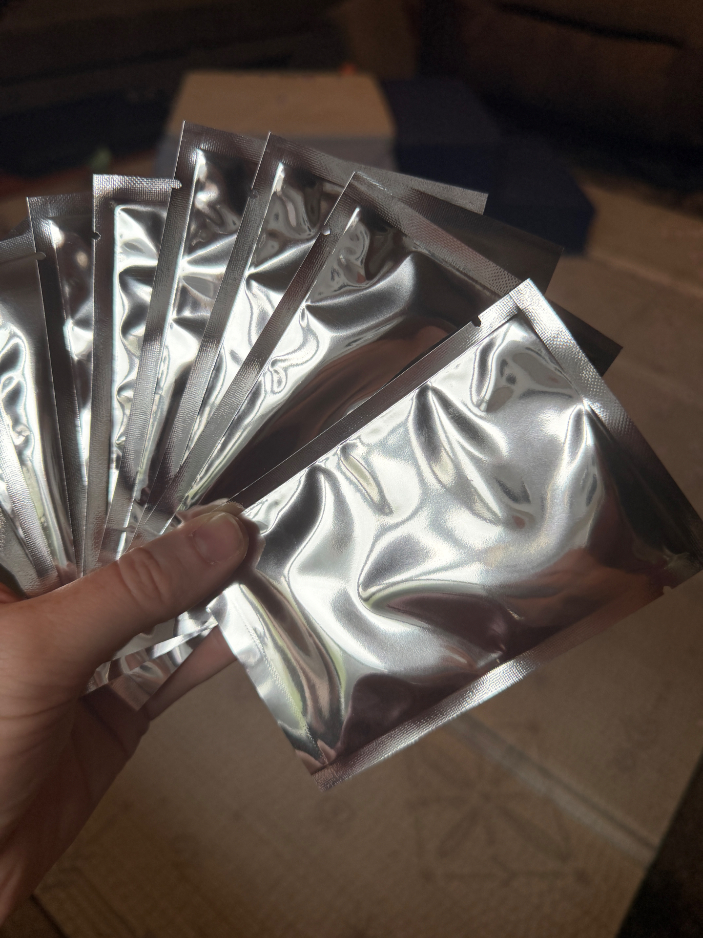 A hand holding a fan of sealed silver foil Faith Creatures packs