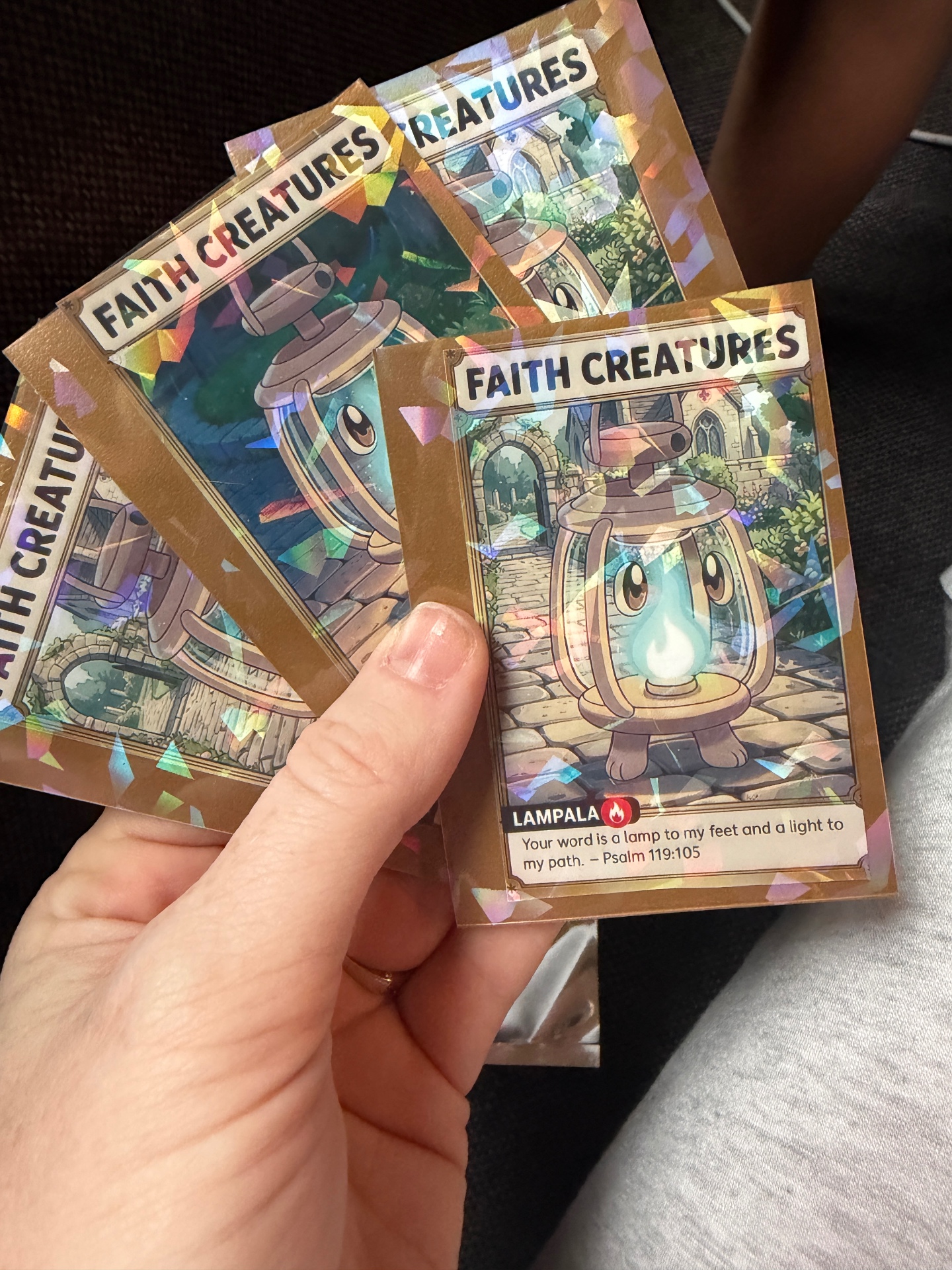 A hand holding three holographic Lampala Faith Creatures cards